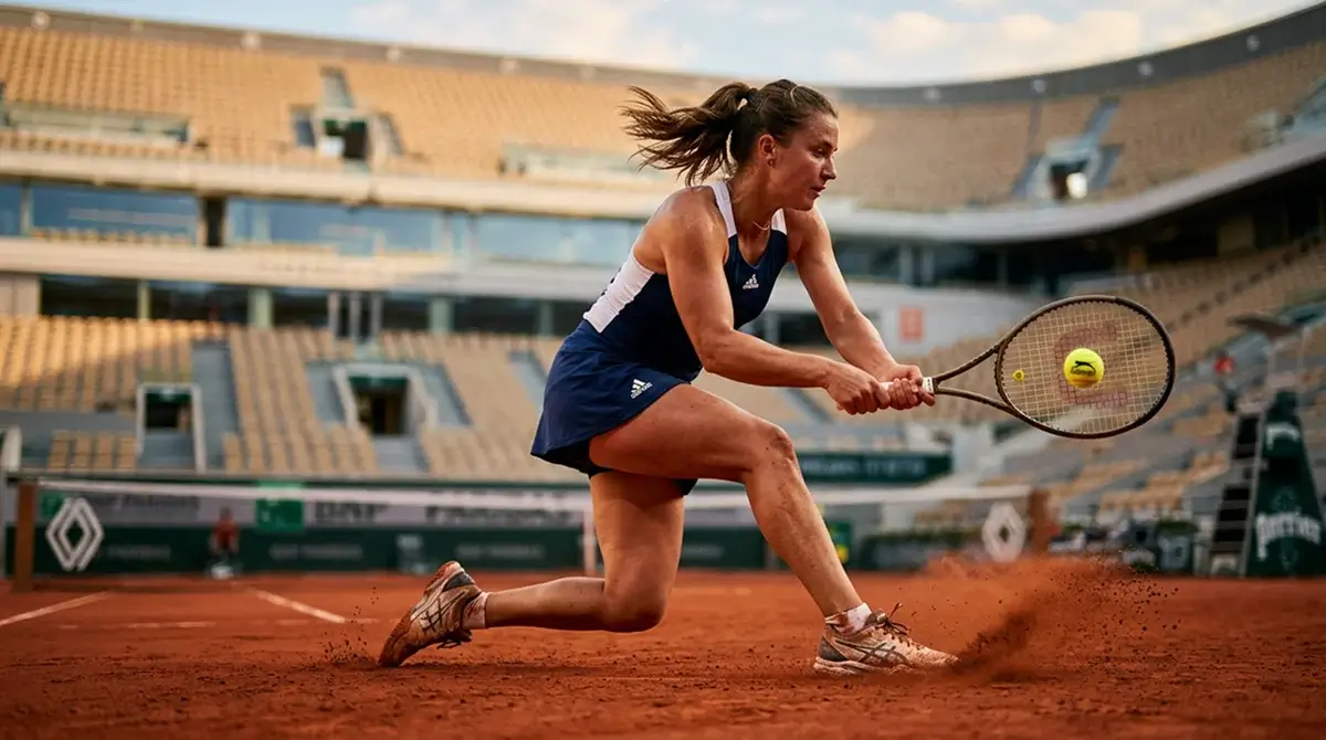A red clay tennis court with a player sliding into a backhand