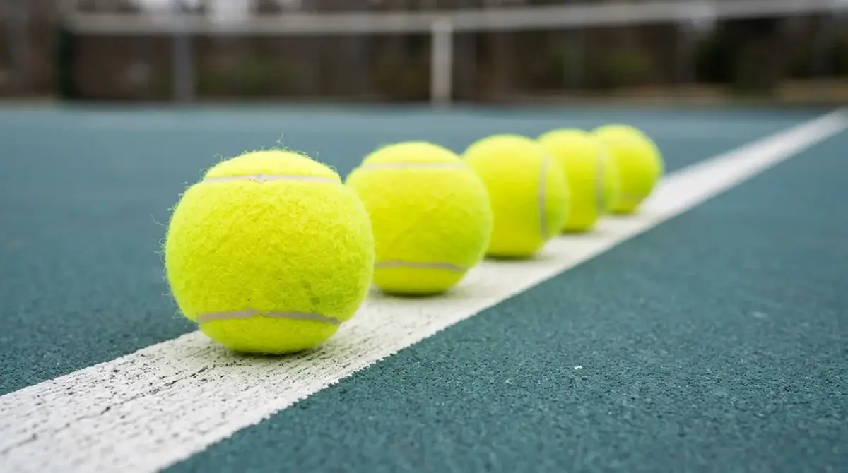A row of tennis balls lined along a court line