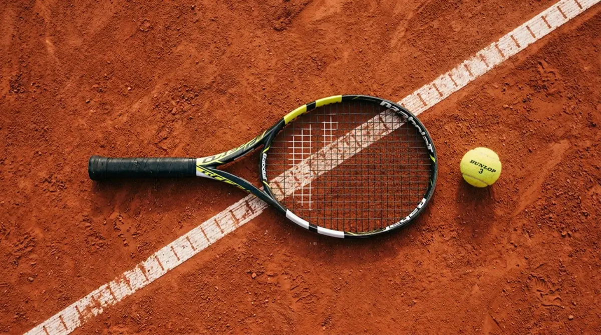 A tennis racket and ball on a clay court before a match