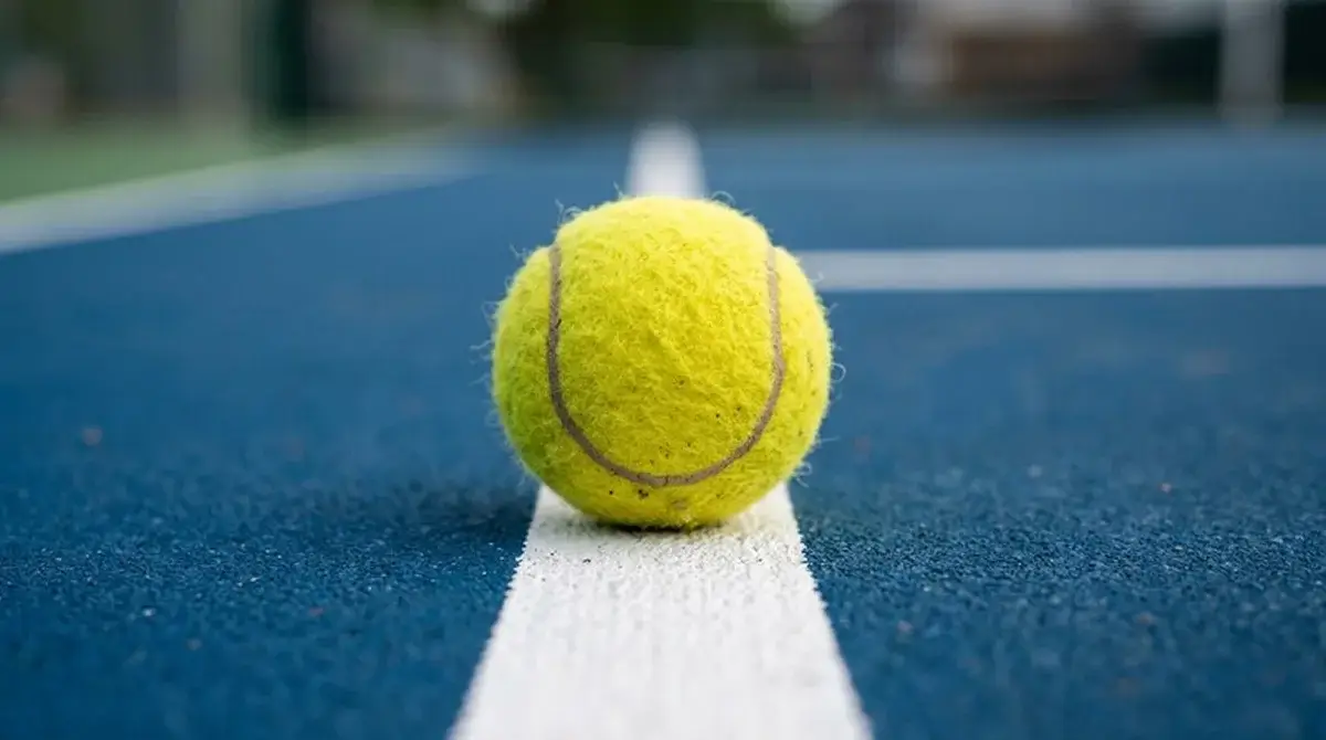 Tennis ball resting on the baseline of a hard court
